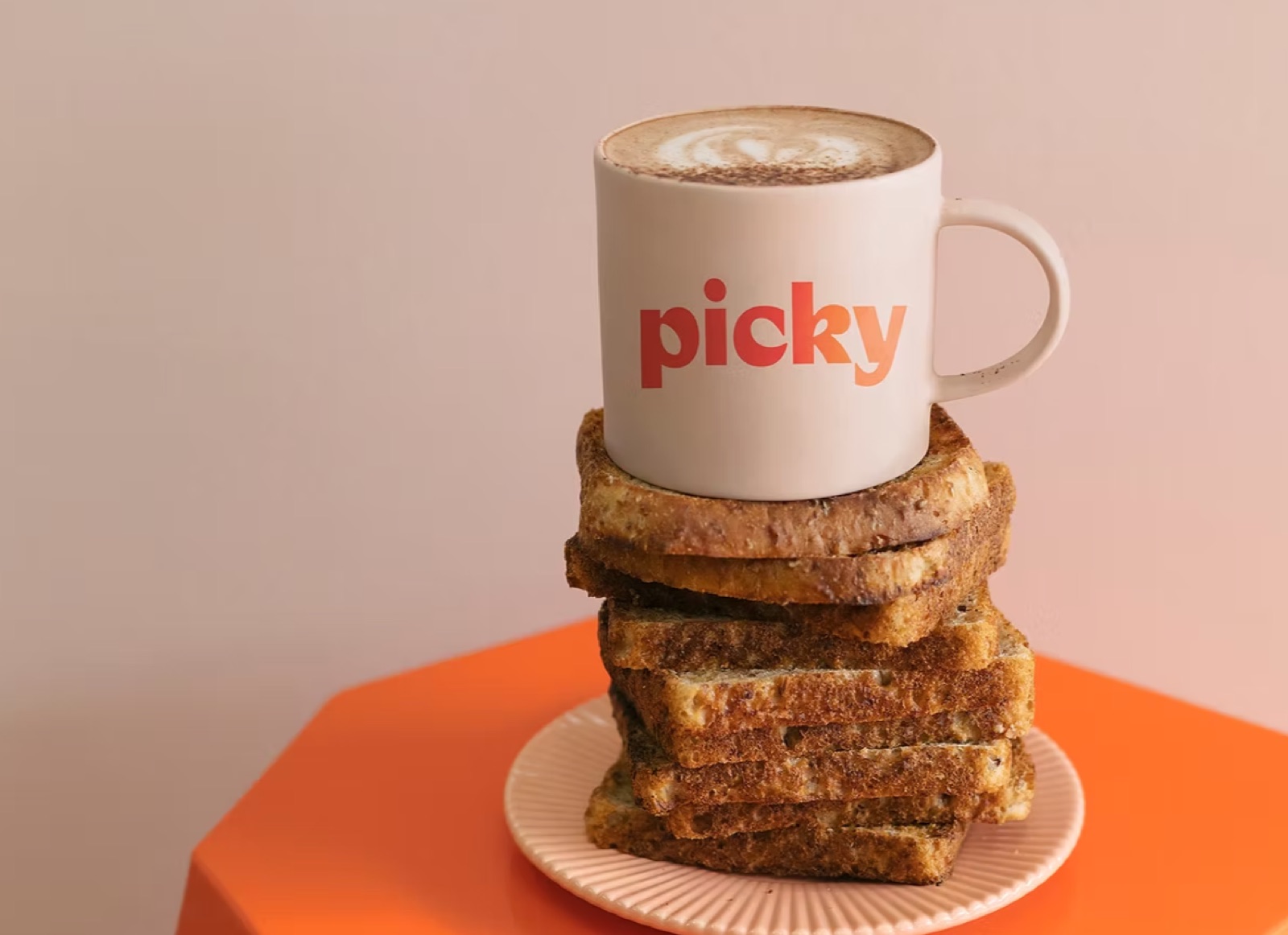 White mug printed with the Picky logo balanced on a stack of toast