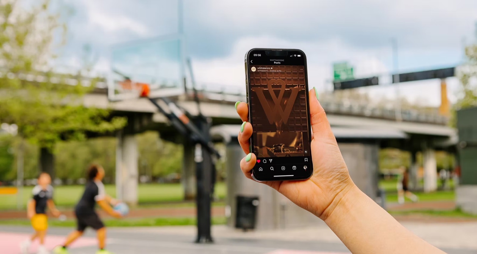 Phone showing a Whittaker's Instagram post with the W logo, held up near a basketball court