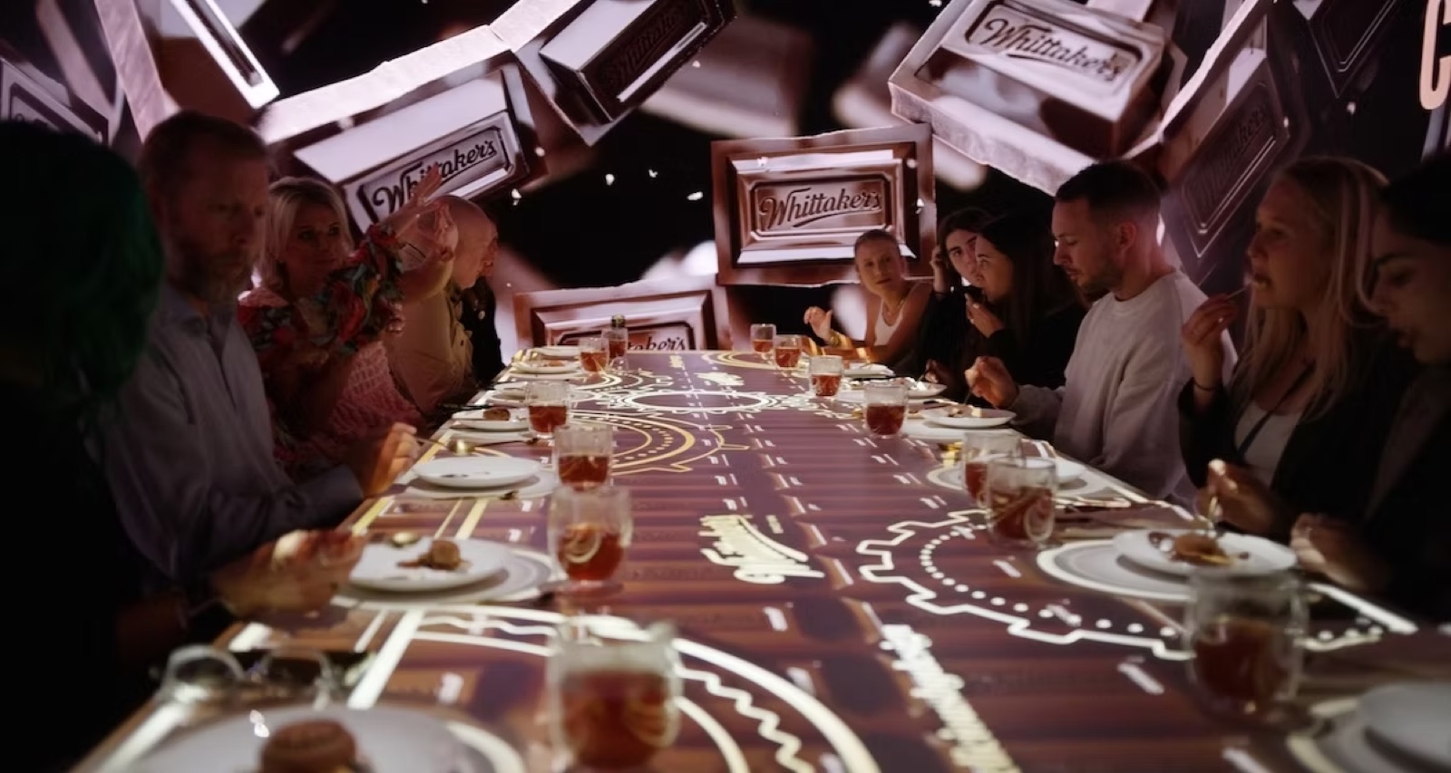 Guests seated at a long dinner table beneath a projection of falling Whittaker's chocolate blocks