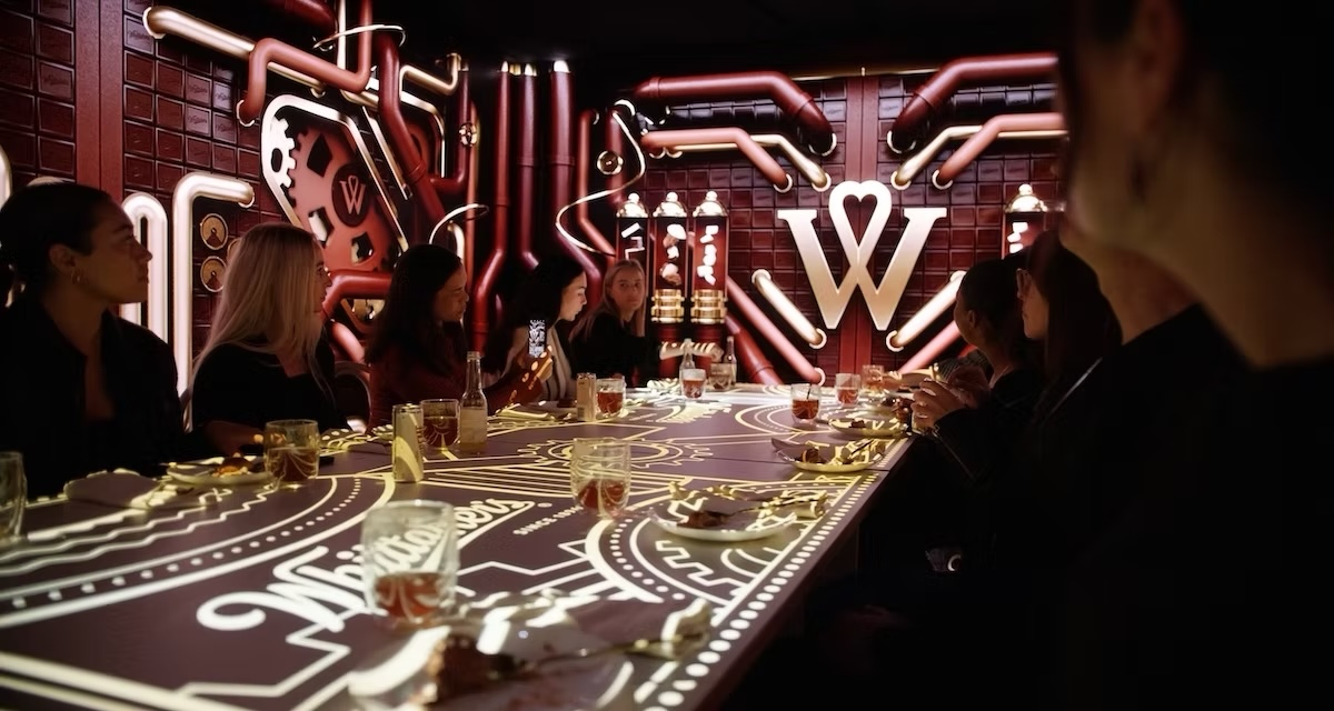 Guests at an immersive Whittaker's branded dinner event lit by a glowing W and pipework installation