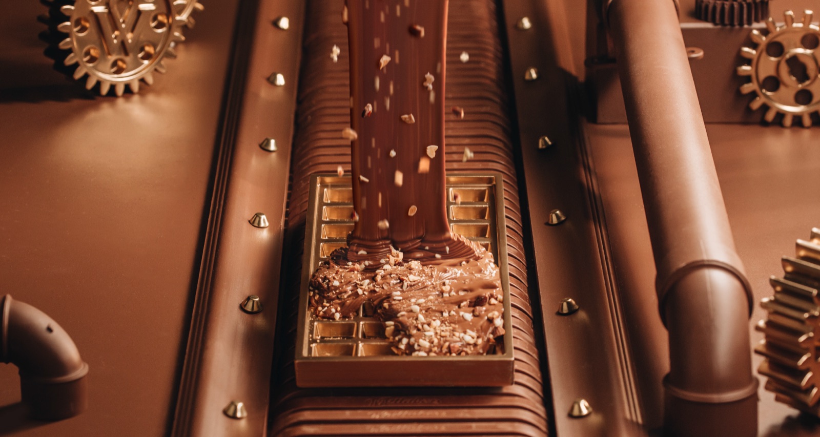 Close-up of melted chocolate poured over a mould with chopped nuts on a chocolate-toned production line set